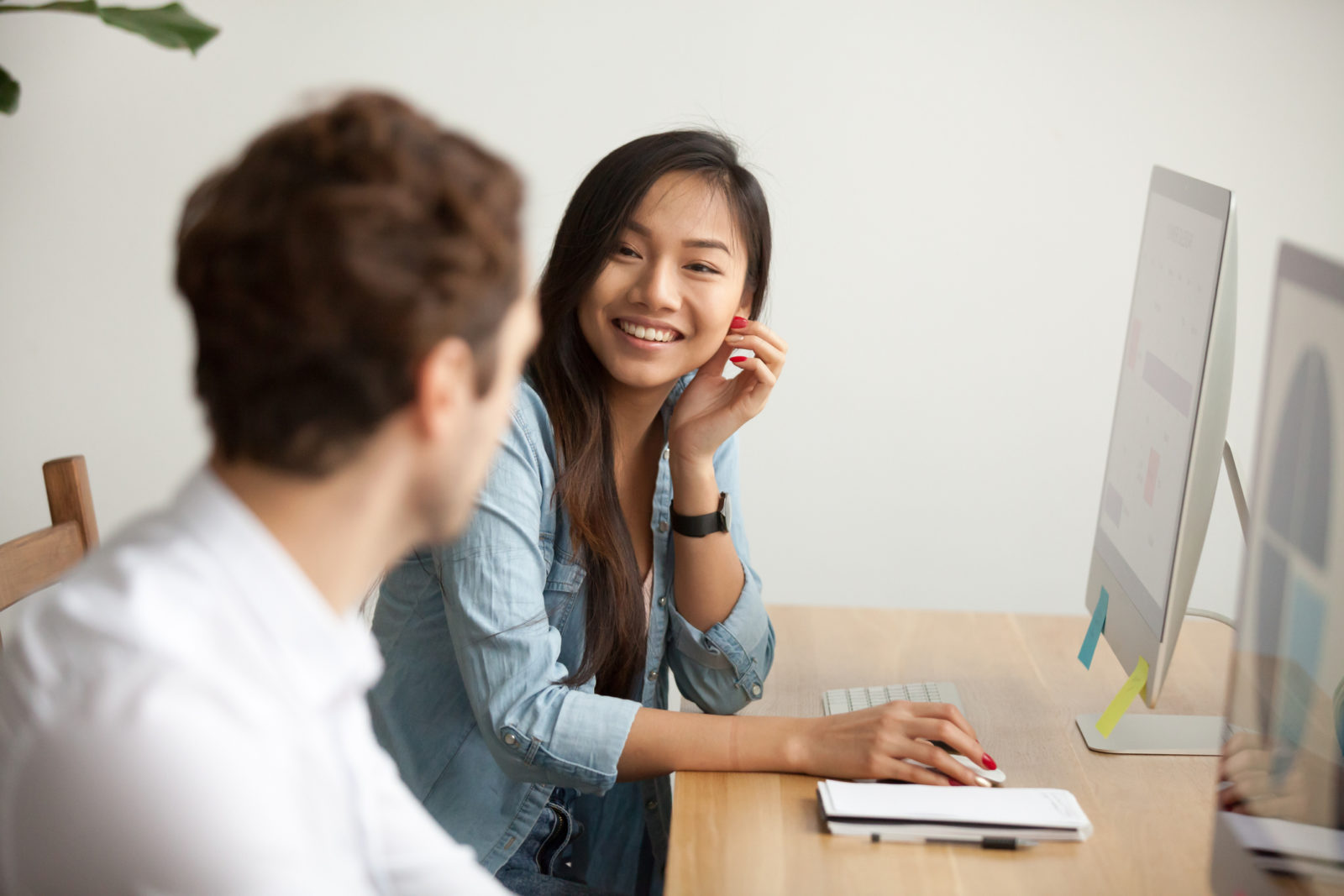 Asain woman smiling at male coworker at desk